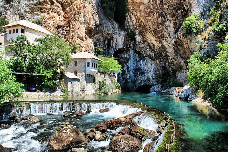 a rock facade nestles a white building next to a sprouting river